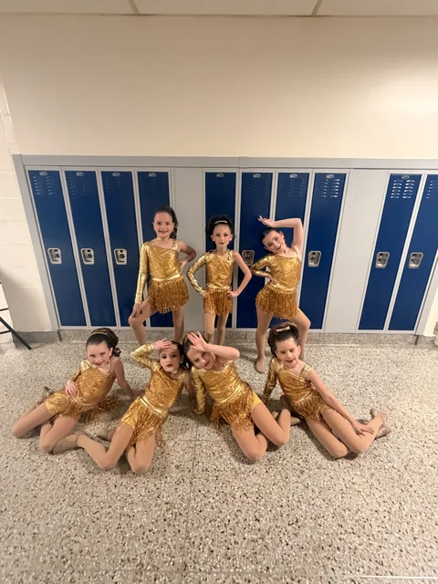 Young dancers in gold costumes posing together backstage