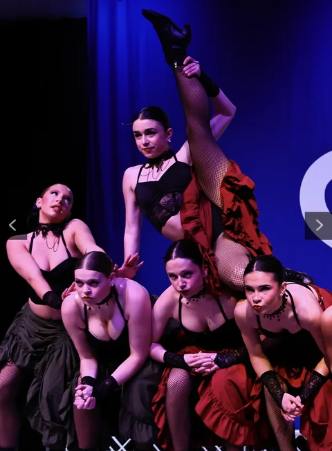 Dance ensemble in black and red costumes holding a group pose