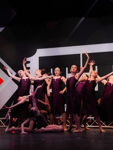 Dancers in purple dresses reaching upward on stage