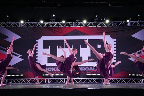 Dancers in purple dresses extending their legs in a coordinated stage performance